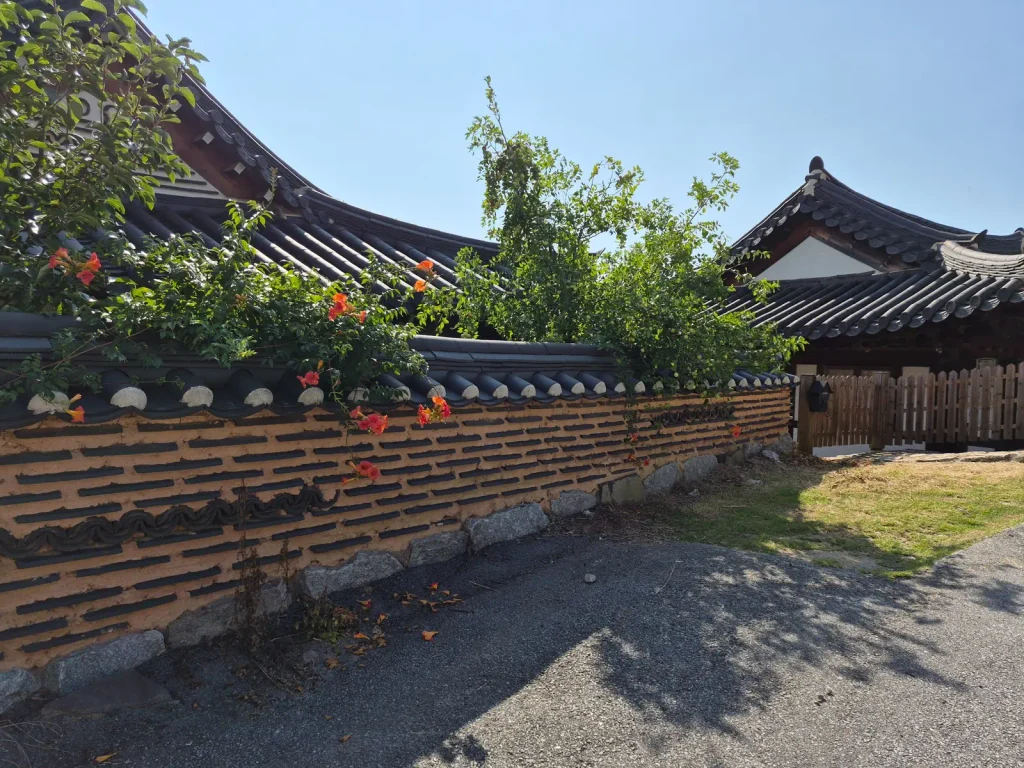 Flowers growing over a traditional Korean earth and tile wall beside hanok houses