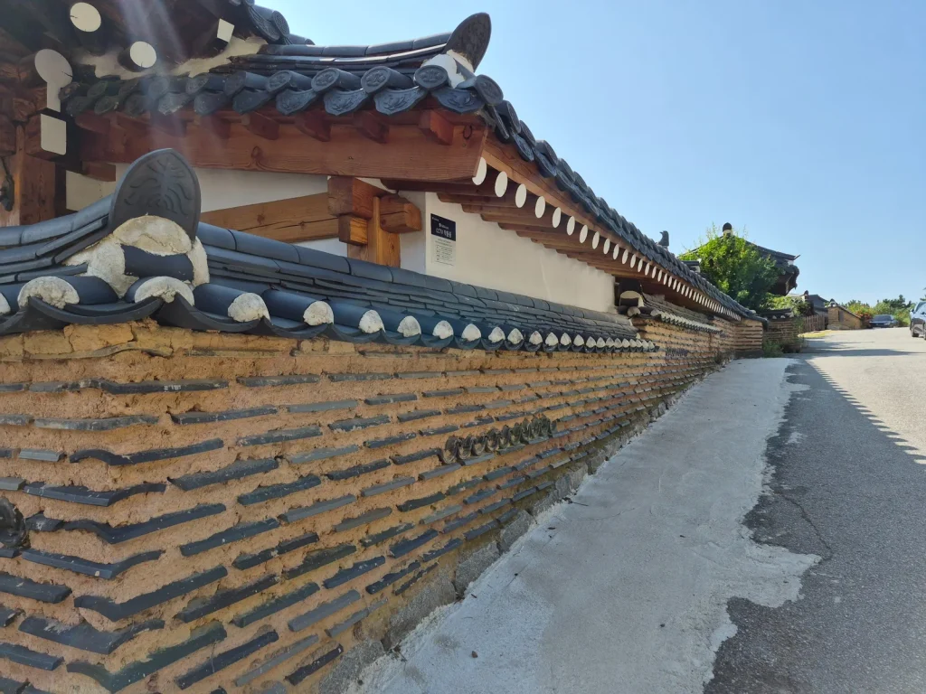 Traditional Korean wall made with earth and rows of roof tile pieces beside a hanok