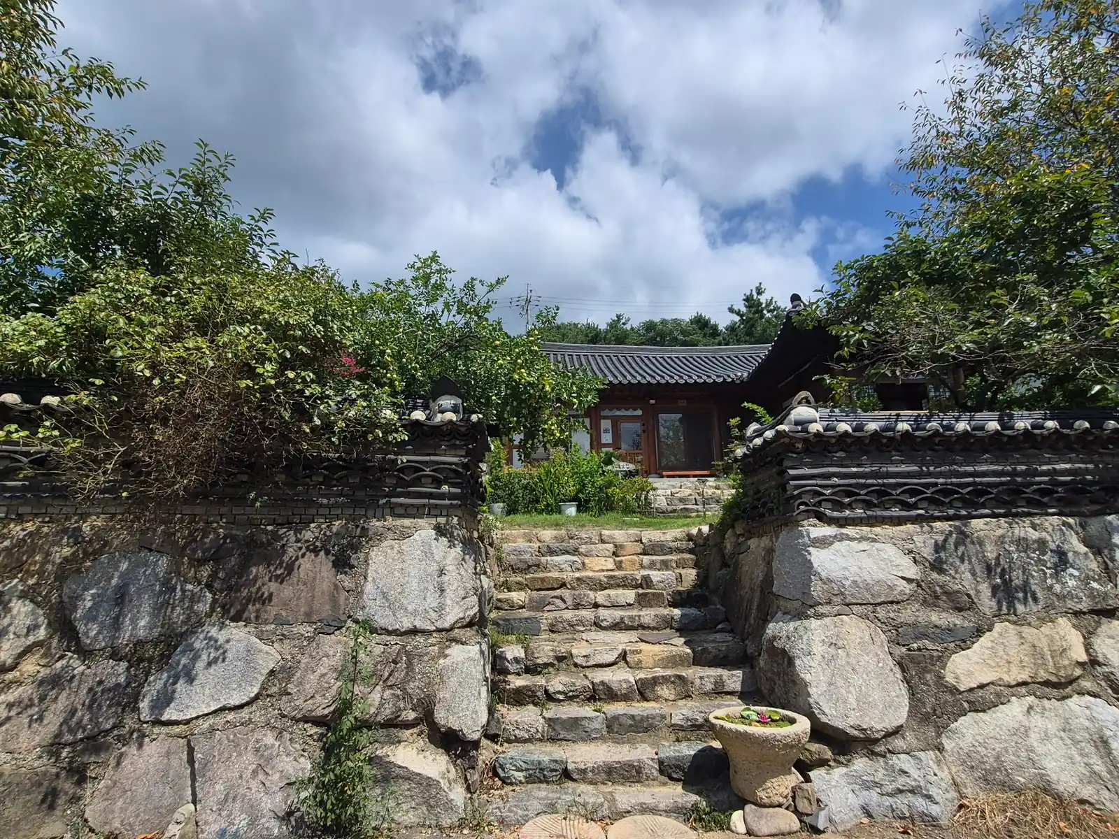Traditional Korean hanok house behind a stone wall and stone steps in rural Korea