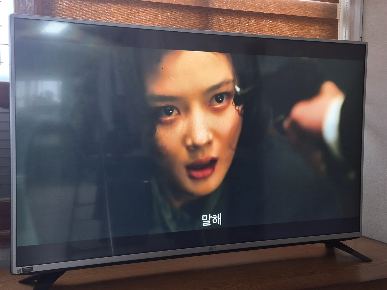 A television in a rural Korean home showing a dramatic close-up from 100 Days of Deception.