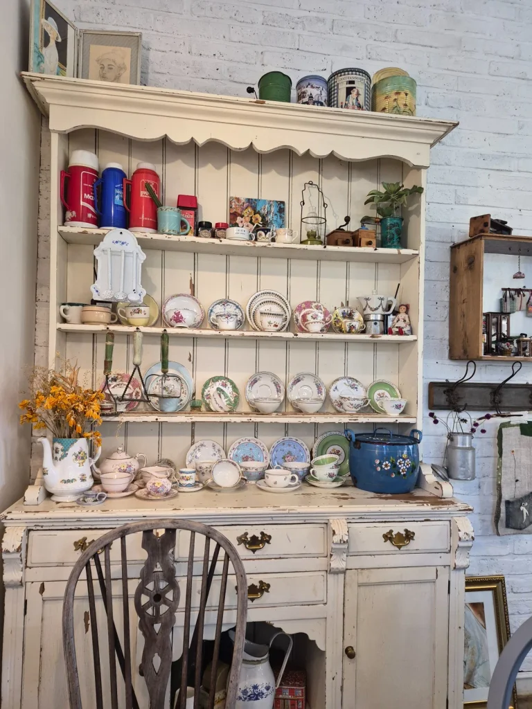 Distressed white wooden cupboard displaying vintage floral teacups, plates and ornaments inside Armeria Café in Gochang