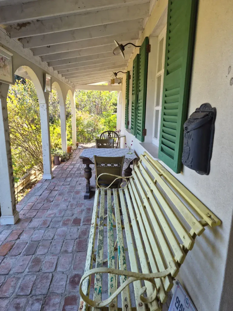 Covered country-house porch with green wooden shutters, a weathered bench and brick flooring at Armeria Café in Gochang