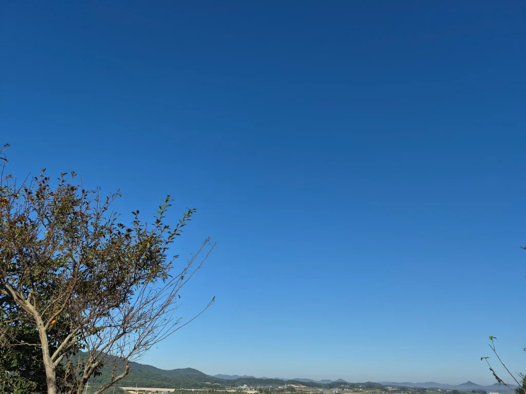 Clear blue autumn sky over trees and distant mountains in rural Korea
