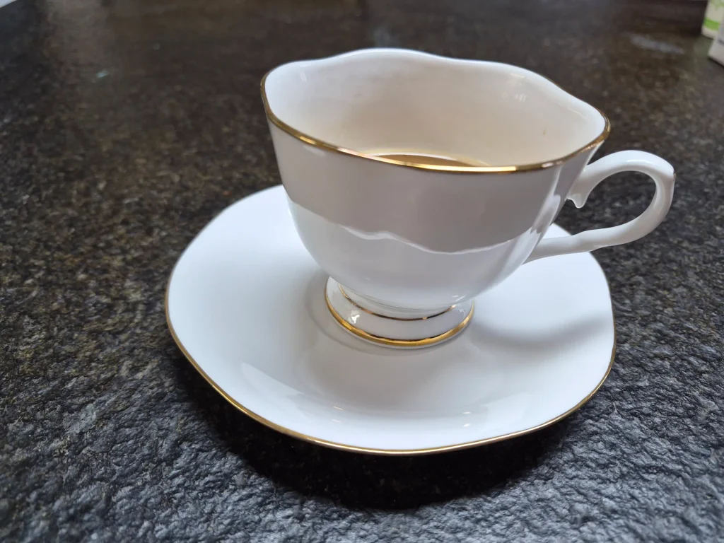 Close-up of a white porcelain coffee cup with gold trim and a matching saucer on a dark countertop