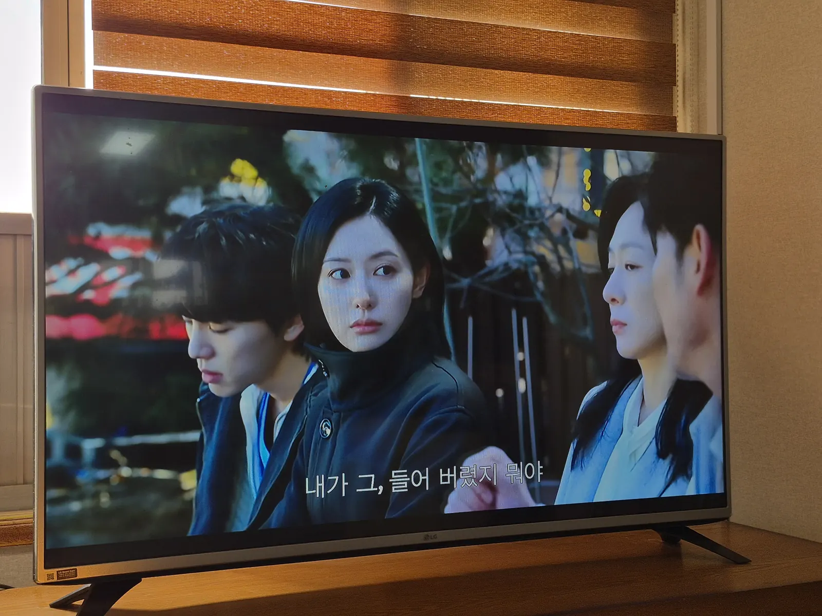 A television showing the Korean medical drama Doctor X in a rural Korean home, with wooden furniture and window blinds.