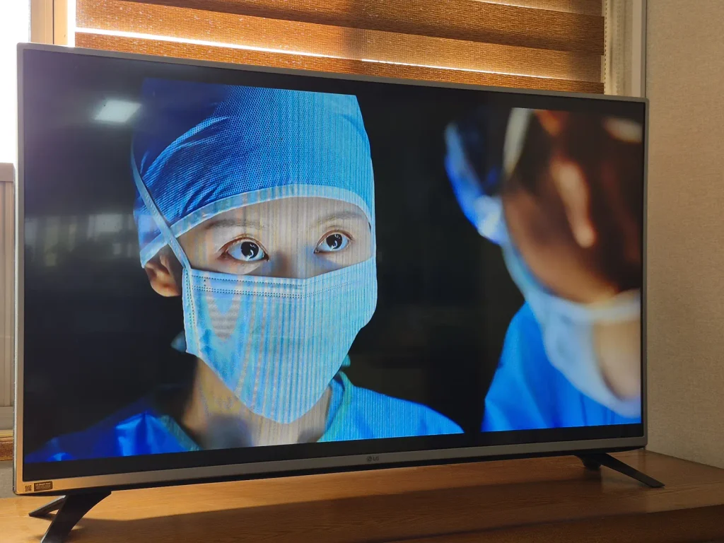A television screen showing a masked female surgeon in blue surgical clothing in the Korean medical drama Doctor X.