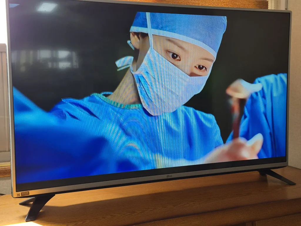 A close-up of a masked surgeon working in an operating room scene from Doctor X, displayed on a television at home.