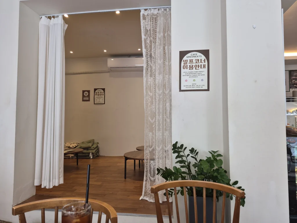 A curtained seating nook at Green Eats with low tables, floor cushions, and a self-service notice on the wall.