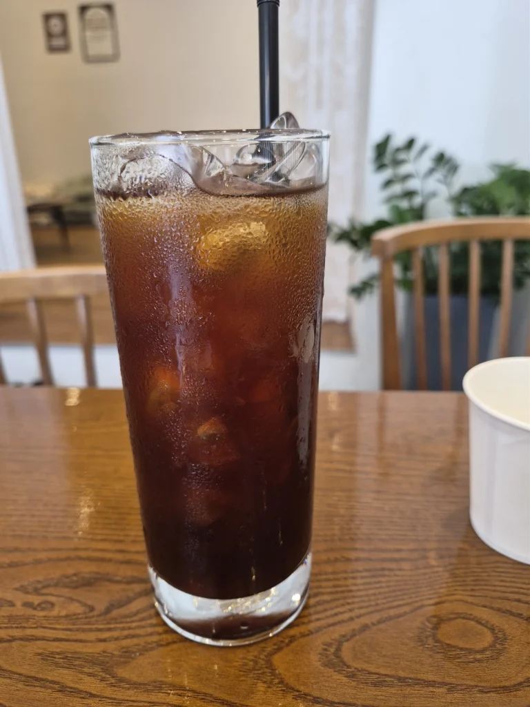 Iced Americano in a tall glass on a wooden table inside Green Eats brunch cafe.