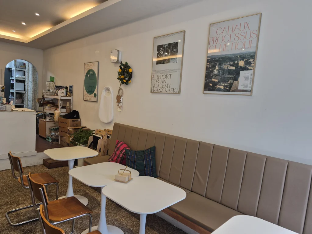 Green Eats interior with a long cushioned bench, white tables, wooden chairs, and framed wall posters.
