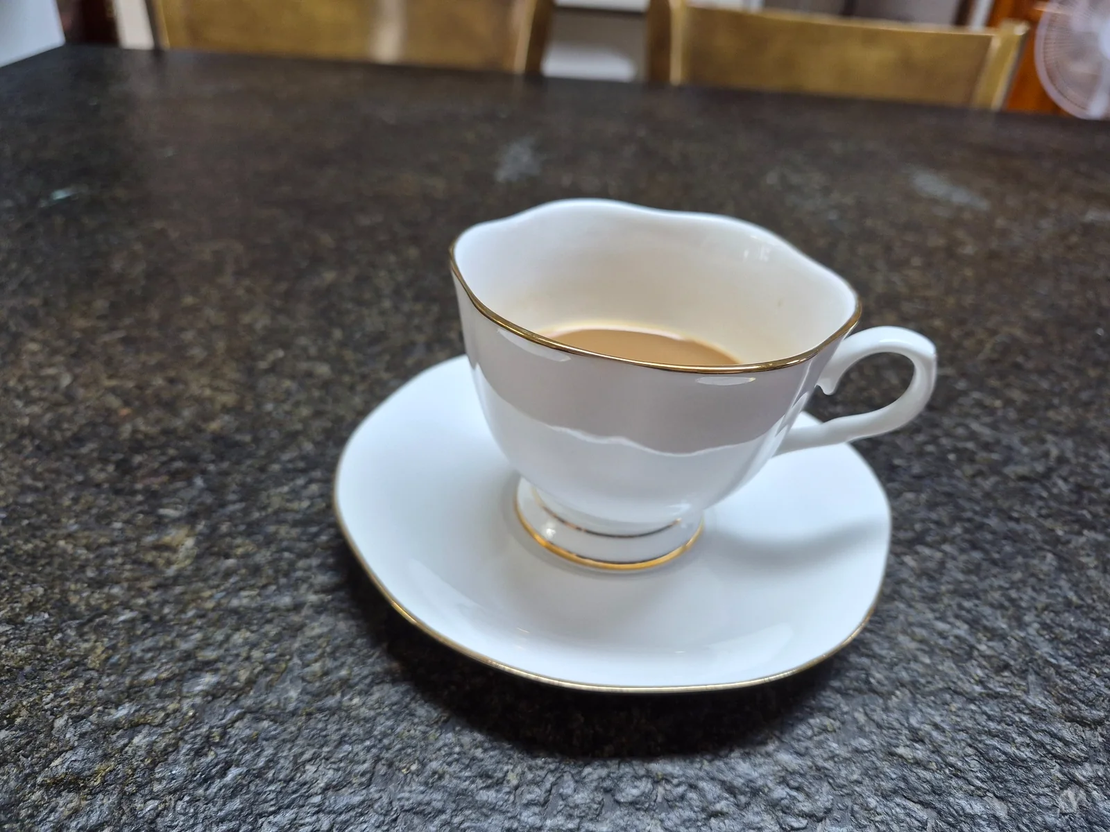 A white coffee cup with gold trim on a dark kitchen counter during a quiet family weekend in rural Korea
